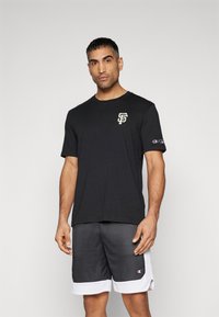 Svart bomull t-skjorte med en hvit og kremfarget "SF" logo på brystet, sammen med svarte mesh-shorts med hvit søm og logo.