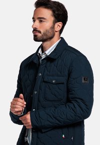 Navy gewatteerde jas van zachte stof, met een knoopsluiting, een borstzak en een logo-embleem op de mouw.