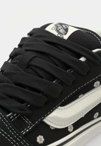 Mustat kanva sneakerit valkoisilla nahkaaksentilla, joissa on silmiinpistäviä kukkakuviota, paksut mustat nauhat ja erottuvat ompelutykset.