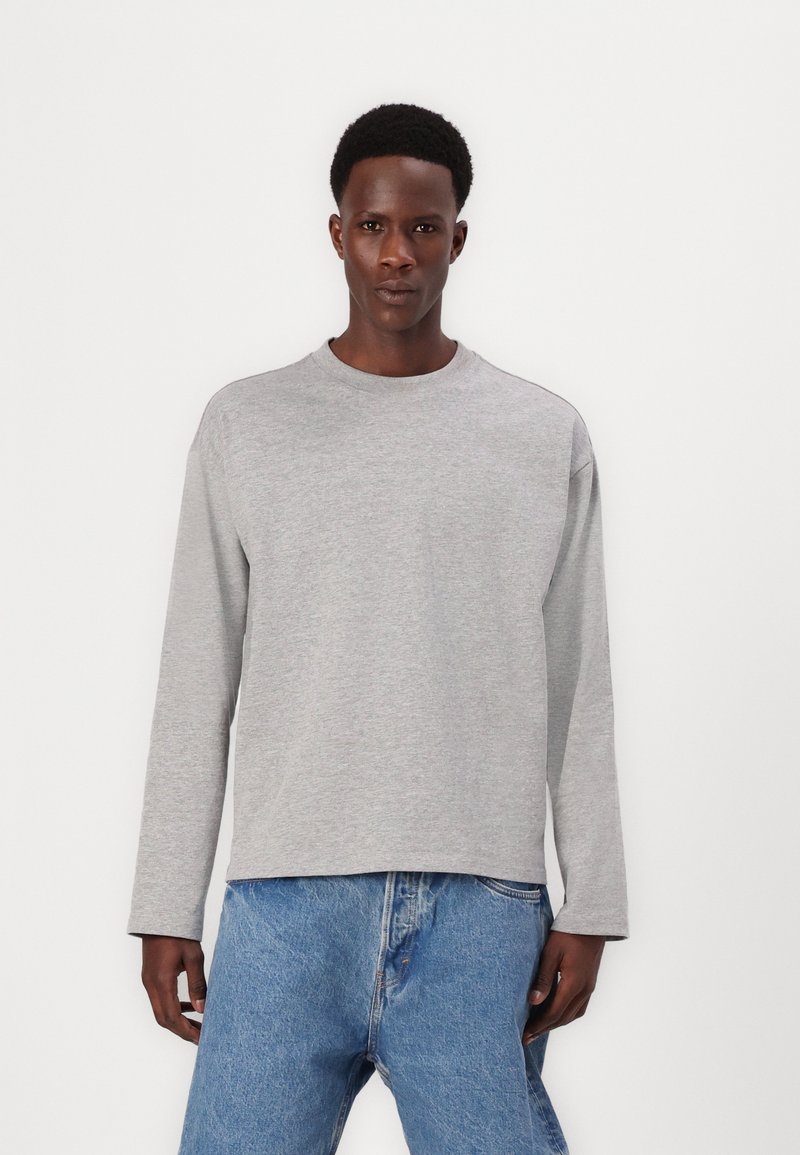 Harmaa pitkähihainen sweatshirt pyöreällä kauluksella, rento istuvuus ja pehmeä tekstuuri. Yhdistetty vaaleansinisiin farkkuihin, joissa on klassinen leikkaus.