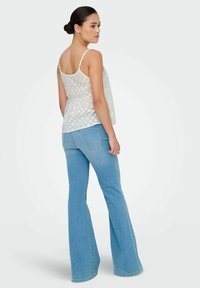 Top blanco sin mangas con un dobladillo peplum y un patrón de diamantes texturizado, combinado con pantalones vaqueros de mezclilla azul claro de corte acampanado con bolsillos traseros.