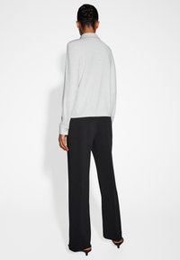 Maglione grigio chiaro, con texture e design con collo, maniche lunghe, abbinato a pantaloni neri a gamba larga e scarpe con tacco.