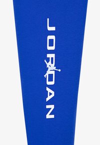 Leggings atléticas azuis com um logo branco "JORDAN" e uma silhueta gráfica. Feitas de um material suave e elástico para conforto e movimentação.