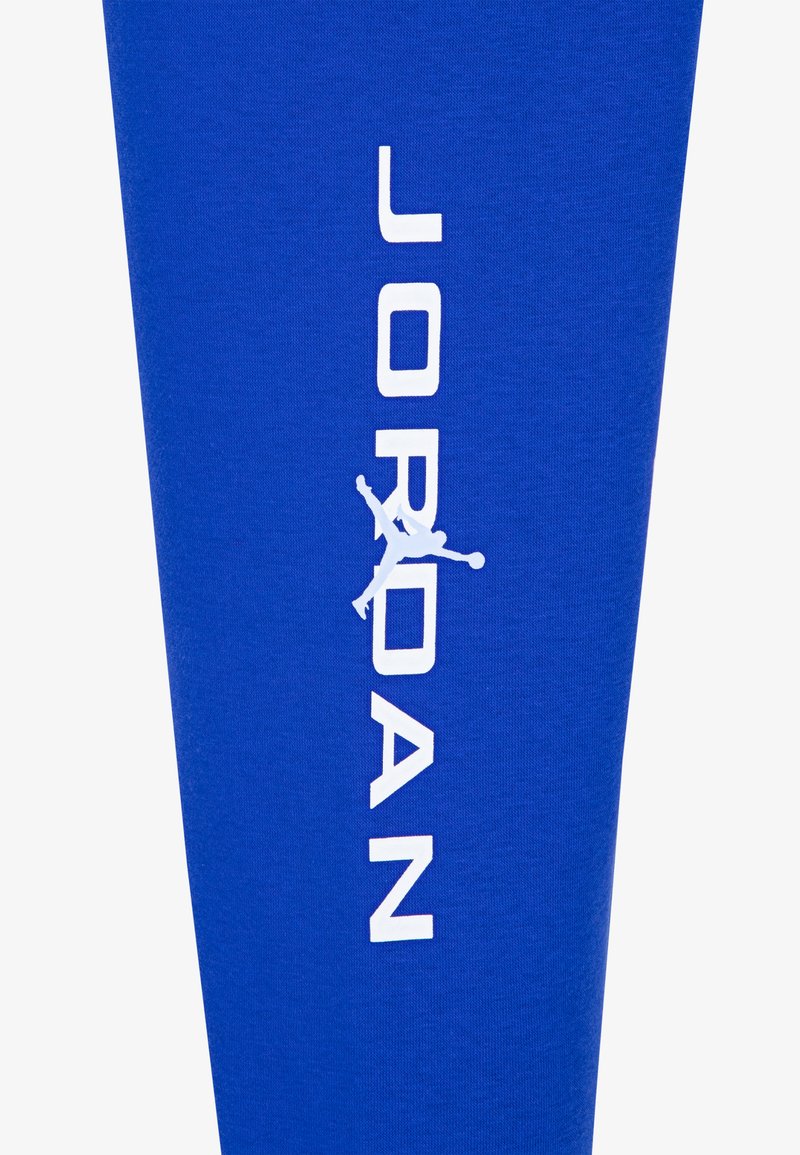 Legging de sport bleu arborant un logo et un graphique en silhouette "JORDAN" blancs. Fabriqué en un matériau doux et extensible pour le confort et la liberté de mouvement.