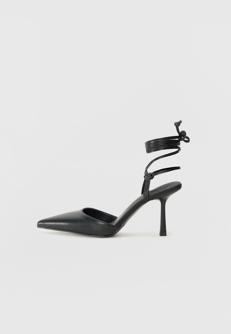 Scarpa nera con punta affusolata e tacco alto, realizzata in pelle liscia e lucida, dotata di un cinturino a spirale per la caviglia e un tacco a stiletto.
