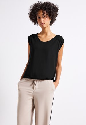 Zwarte top met korte mouwen en een ronde hals, gecombineerd met beige broek met trekkoorden en een zwarte streep aan de zijkant. Glad, lichtgewicht materiaal.