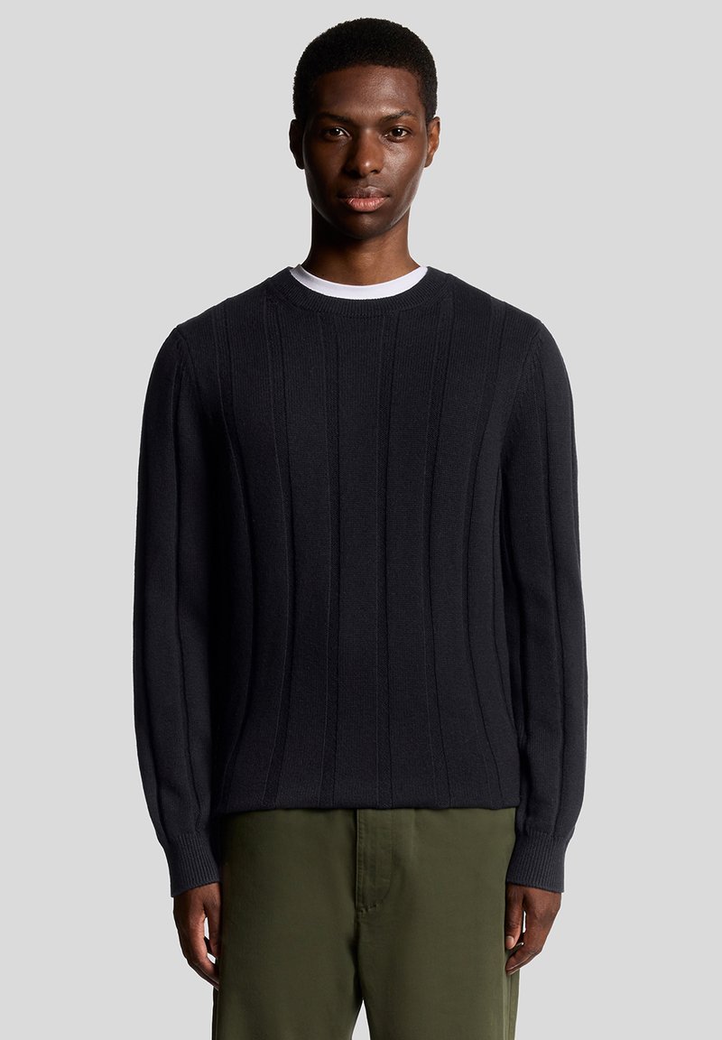 Dunkelblauer, gerippter Pullover mit Rundhalsausschnitt, vertikalen Nähten und langen Ärmeln, kombiniert mit olivgrünen Hosen. Glatte Textur.