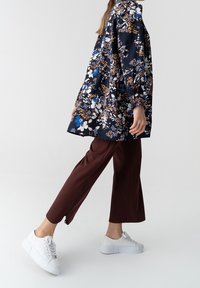 Kwiatowa granatowa kurtka z długimi rękawami i luźnym krojem, zestawiona z brązowymi spodniami o długości 3/4 z bocznymi zameczkami i białymi sneakersami.