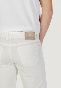 Jeans blancos con una etiqueta de cuero que dice "JECKERSON" en la parte trasera, con dos bolsillos traseros y detalles de costura visibles.