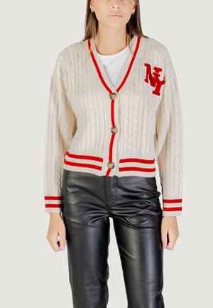 Cardigan en tricot beige avec des bords contrastants rouges, présentant une texture en tricot à cable, trois boutons et un logo 'NY' brodé sur la poitrine.