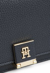 Schwarze strukturiertes Lederhandtasche mit einer goldfarbenen Logo-Schnalle, rechteckiger Form und schlankem Design mit subtilen Details.
