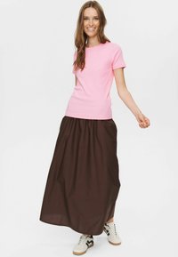 Tricou roz cu mânecă scurtă asortat cu o fustă lungă maro, confecționată dintr-un material ușor, completată cu teniși albi cu accente negre.