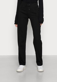 Pantalones de chándal negros con corte relajado, que cuentan con una cintura con cordón y bolsillos laterales con cremallera. Textura suave y diseño de pierna recta.