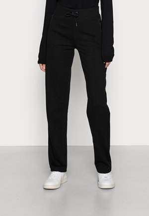 Pantalones de chándal negros con corte relajado, que cuentan con una cintura con cordón y bolsillos laterales con cremallera. Textura suave y diseño de pierna recta.