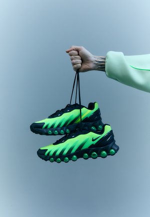 Baskets Nike noires et vert fluo, avec une tige en mesh, un design courbé et une semelle distinctive rembourrée avec des accents sphériques.