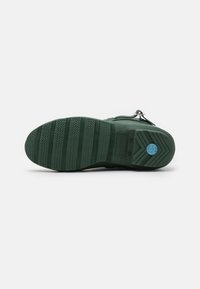 Suela de zapato de goma verde con un patrón de textura y surcos horizontales y verticales, logo en relieve y un diseño de tacón elevado.