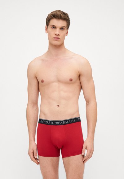 Piros pamut boxer alsónemű fekete gumiszalaggal, amelyen az "Emporio Armani" logó található, testhezálló kialakítással és sima textúrával.