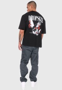 Black graphic t-shirt featuring a white print with birds and roses on the back. Paired with gray cargo pants and white sneakers.