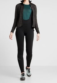 Svarta tights i figurnära modell, kombinerade med en mörkgrå zip-up jacka och en turkos topp. Funktioner inkluderar en elegant design, lätt material och subtila detaljer.