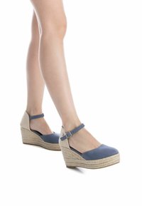 Zapatos de cuña con parte superior azul en material suave. Presentan un tacón beige texturizado y una correa al tobillo con un hebilla plateada para un ajuste seguro.