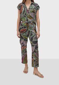 Pestrobarevný overál s klopovým zapínáním a stahovacími šňůrkami v pase. Obsahuje odvážné vzory listů na tmavém pozadí. Ploché sandály.