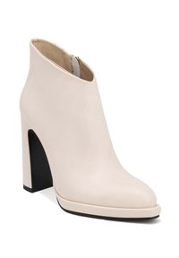 Stivaletto beige con tacco alto, finitura in pelle liscia, punta affusolata, chiusura con zip frontale e tacco a blocco nero a contrasto.