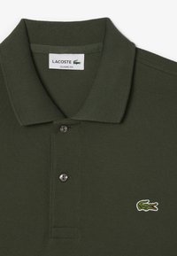 Mörkgrön pikétröja med ribbad krage, utrustad med två silverfärgade knappar och en broderad grön krokodil logo på bröstet. Klassisk passform.