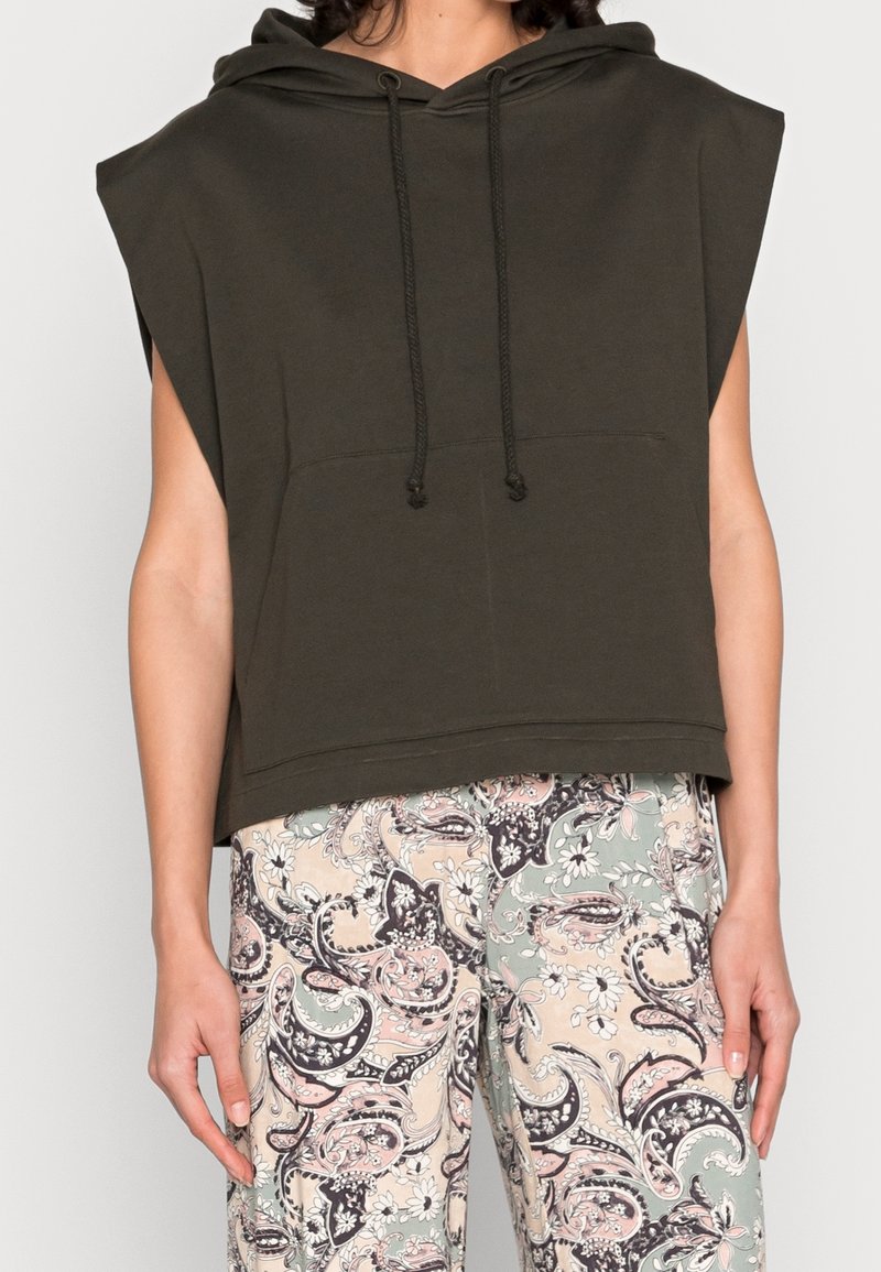 Bezrukávý tmavě zelený kapucňák s tkaničkami, doplněný o kalhoty s vysokým pasem s pastelovým paisley a květinovým motivem.