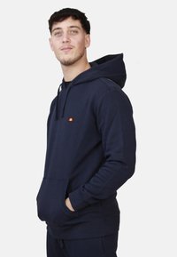 Felpa con cappuccio blu navy in morbido tessuto; presenta una tasca a marsupio, polsini a coste e un piccolo logo sul petto.