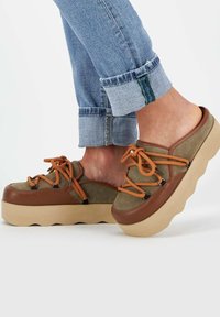 Scarpe platform verdi e marroni con dettagli color tan e lacci arancioni; progettate con una punta arrotondata e una suola texturizzata per una presa migliore.