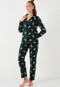 Conjunto de pijama verde de canalé que incluye una camisa con botones y pantalones largos, adornado con un patrón floral en rojo y blanco, de textura suave.
