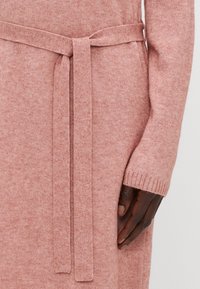Abito lavorato a maglia rosa con una cintura in vita. Il tessuto sembra morbido e testurizzato, con polsini a coste e un design senza cuciture.