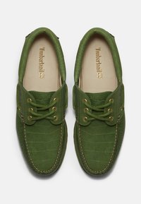 Chaussures en cuir vert de style mocassin avec un motif texturé, lacets à l'avant, semelles intérieures beiges et logo Timberland à l'intérieur.