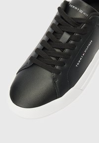 Crni Tommy Hilfiger tenisice s teksturiranim kožnim gornjištem, crnim vezicama, bijelim potplatom i logotipom sa strane i na jeziku.