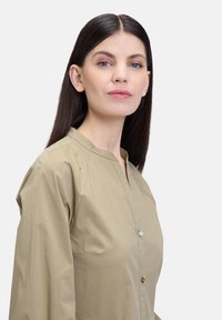 Kahki Button-up Hemd mit Stehkragen, glatter Textur und leichtem Glanz, das einen sauberen, maßgeschneiderten Schnitt aufweist.