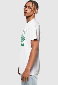 T-shirt en coton blanc avec un graphique de spaghetti vert et du texte. Manches courtes, coupe décontractée, texture lisse et encolure ras du cou standard.