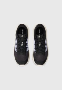 Baskets de sport noires avec une tige en mesh respirant, accents en zigzag blancs, lacets plats et une semelle intermédiaire blanche rembourrée.