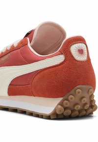 Piros és rózsaszín sneaker, velúrból és szintetikus anyagokból készült, fehér csíkkal, részletes sarokpárnával és gumitalppal, amely körkörös taposókkal rendelkezik.