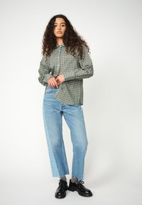 Green long-sleeve shirt with white polka dots, paired with light blue straight-leg jeans, and black lace-up shoes.