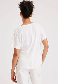 T-shirt bianco a maniche corte con vestibilità comoda, tessuto morbido e collo a giro. Dettagli delle cuciture visibili sul retro e sulle maniche.