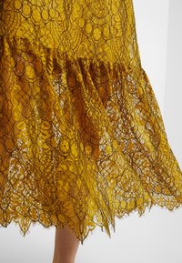 Vestido de encaje amarillo con intrincados patrones florales, dobladillo con volantes y textura translúcida, con costuras negras detalladas en toda la prenda.