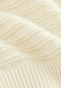 Knit-kangas, joka on tekstuuriltaan kermaista ja sisältää aaltoilevia kuvioita sekä ribattuja yksityiskohtia, esittelee pehmeitä kuituja, jotka luovat mukavan ilmeen.