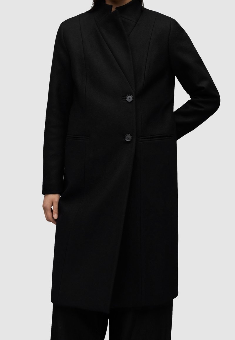 Czarny wełniany płaszcz o dopasowanym kroju, z wysokim kołnierzem i dwoma guzikami z przodu. Posiada boczne kieszenie i gładką fakturę.