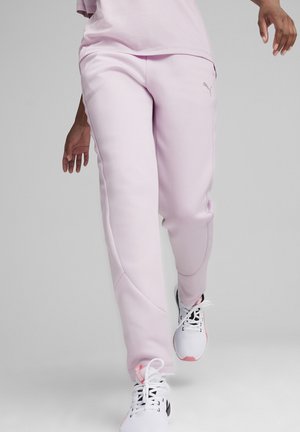 Helle rosa Jogginghose mit glatter Textur, seitlichen Nähten und einem Logo-Detail. Getragen mit weißen Sportschuhen mit pinken Akzenten.