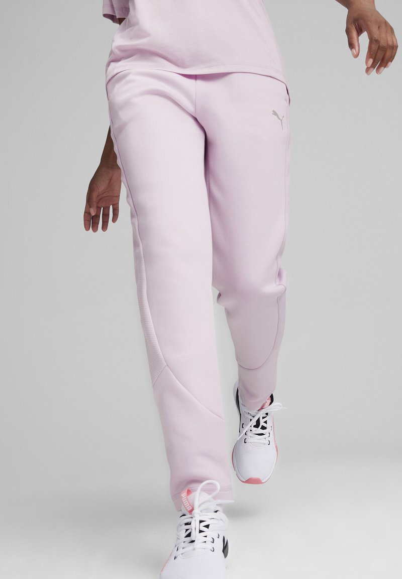 Svetlo roza trenerke z gladko teksturo, stranskimi šivi in detaljem logotipa. Nosi se z belimi atletski čevlji z roza akcenti.