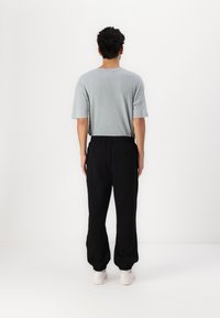 Grå kortærmet t-shirt parret med sorte sweatpants med elastisk talje og afsluttede ankler, sat mod en ensfarvet hvid baggrund.