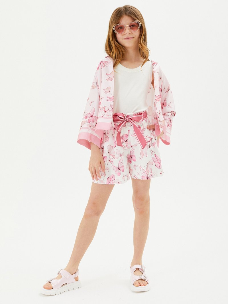 Outfit rosa chiaro con stampa di farfalle, composto da una giacca corta e pantaloni shorts, abbinato a sandali rosa e occhiali da sole a forma di cuore.