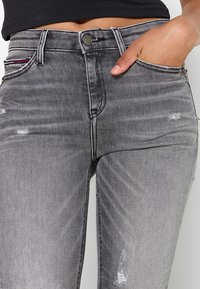 Pantalones vaqueros de mezclilla gris con un acabado desgastado, detalles desgastados cerca de los bolsillos y costuras en contraste. Diseño de cintura alta con cinco bolsillos convencionales.