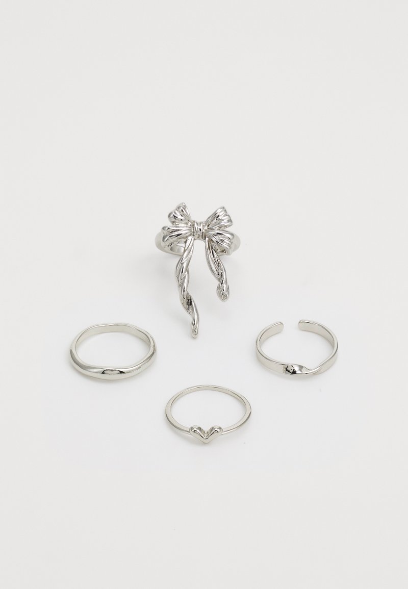 Conjunto de anillos de plata con un diseño en forma de lazo, tres bandas lisas, una de ellas con un detalle de corazón y varias formas de anillo, todo con acabado pulido.