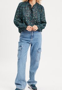 Blouse à motif paisley vert avec des poignets smockés, assortie à un jean cargo bleu clair avec poches latérales et une coupe d�écontractée.